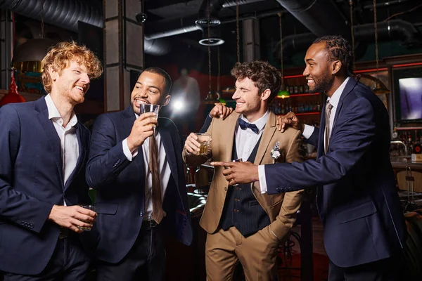 Heureux interracial meilleurs hommes en tenue formelle félicitant ami dans le bar, les hommes avec des lunettes de whisky — Photo de stock