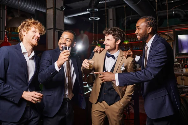 Happy interracial best men in formal wear congratulating friend in bar, men with glasses of whiskey — Stock Photo
