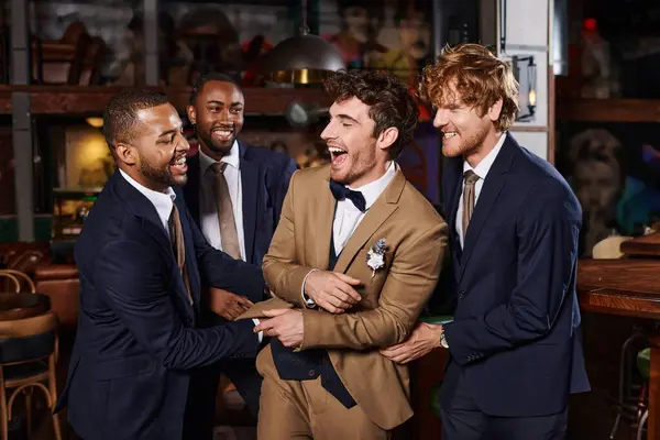 Despedida de soltero, excitado interracial hombres felicitando amigo en bar, mejores hombres y novio en trajes - foto de stock