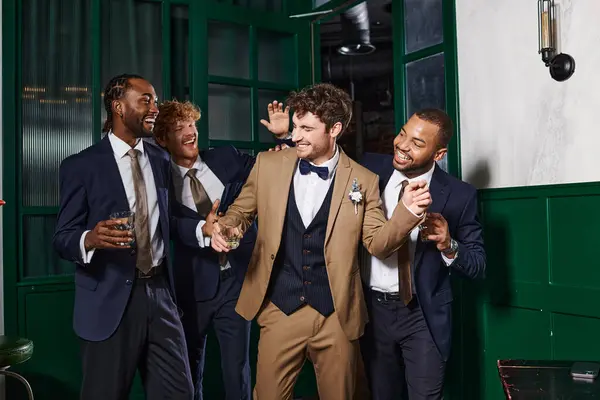 Enterrement de vie de garçon, meilleurs hommes et mariés multiethniques riant en se tenant debout avec des verres de whisky — Photo de stock