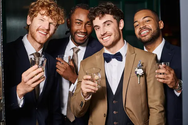 Bachelor party, portrait of happy multiethnic best men and groom standing with glasses of whiskey — Stock Photo