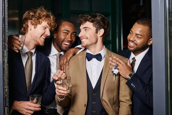 Despedida de soltero, retrato de los mejores hombres interracial feliz y novio de pie con vasos de whisky - foto de stock