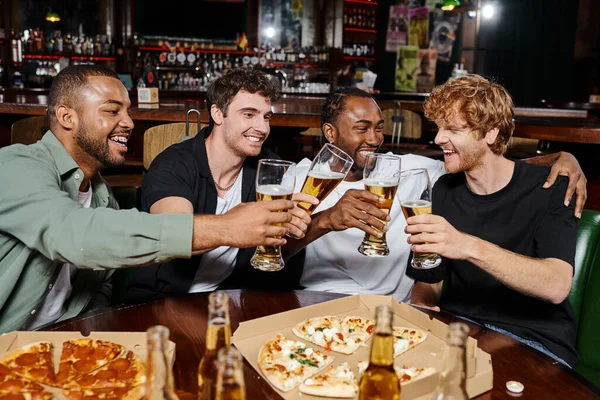 Serata fuori, gioiosi uomini multietnici che si accarezzano bicchieri di birra vicino alla pizza nel bar, amicizia maschile — Foto stock