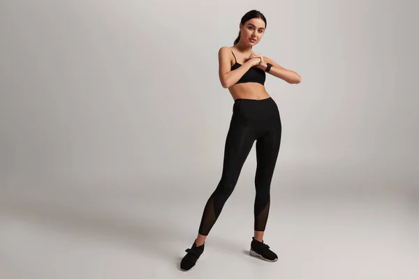 Joven mujer deportiva en ropa deportiva negra con rastreador de fitness en la muñeca haciendo ejercicio sobre fondo gris - foto de stock