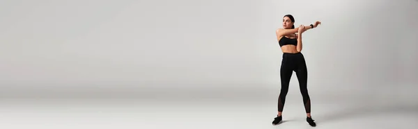 Спортивна жінка в чорному спортивному одязі з фітнес-трекером на зап'ясті, що тягнеться на сірому тлі, банер — стокове фото