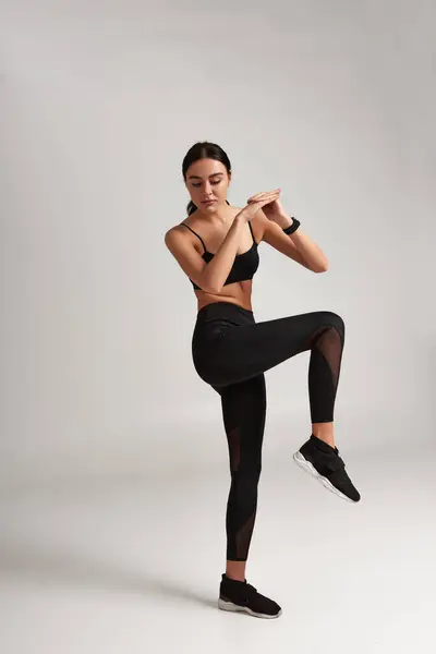 Mulher muito desportiva em sportswear preto com rastreador de fitness no pulso aquecendo em pano de fundo cinza — Fotografia de Stock