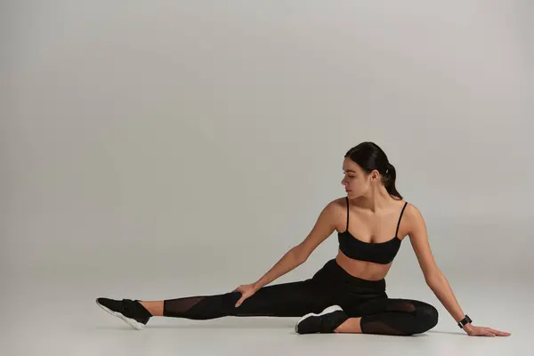 Mulher flexível e apto no desgaste ativo e tênis esticando as pernas no fundo cinza, motivação — Fotografia de Stock