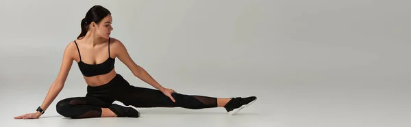 Femme flexible en tenue active et baskets étirant les jambes sur fond gris, bannière de motivation — Photo de stock