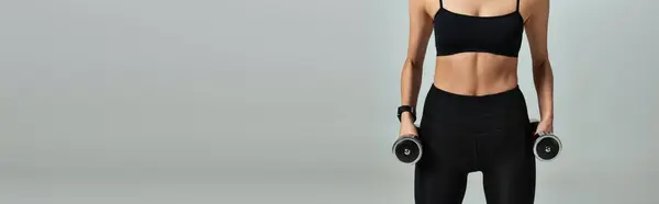 Cropped view of sportswoman in black active wear exercising with dumbbells on grey backdrop, banner — Stock Photo