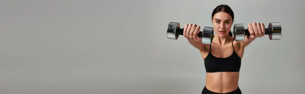 Motivated sportswoman in black active wear working out with dumbbells on grey backdrop, banner — Stock Photo