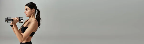 Vue latérale de la jeune femme sportive en haltères de levage d'usure active sur fond gris, bannière — Photo de stock