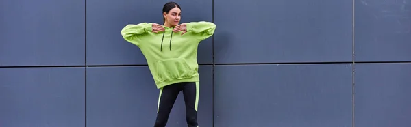 Sportlerin in Kapuzenpulli und Leggings wärmt sich an grauer Wand im Freien auf, frische Luft und Sportbanner — Stock Photo