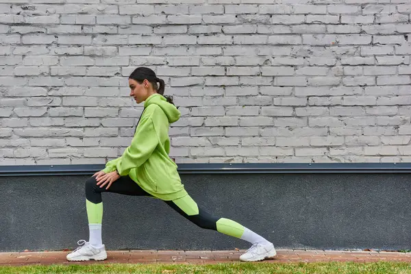 Pretty young sportswoman in lime color hoodie and leggings doing lunges before running outdoors — Stock Photo