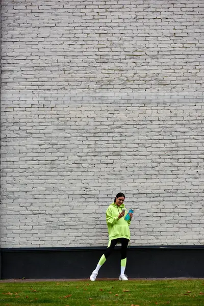Sportive heureuse en sweat à capuche et leggings à l'aide d'un smartphone et debout avec bouteille d'eau — Photo de stock