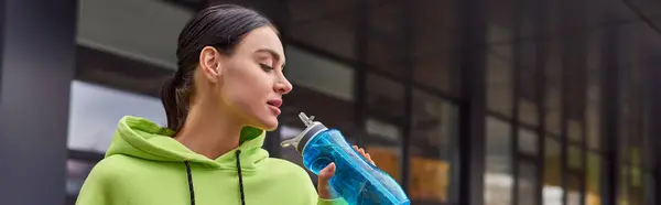 Pretty sportswoman in lime color hoodie drinking water from bottle after workout, horizontal banner — Stock Photo