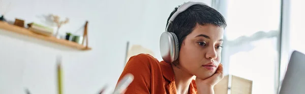 Enfocada mujer de pelo corto sosteniendo la pluma y mirando atentamente a su computadora portátil, estudiando, pancarta - foto de stock