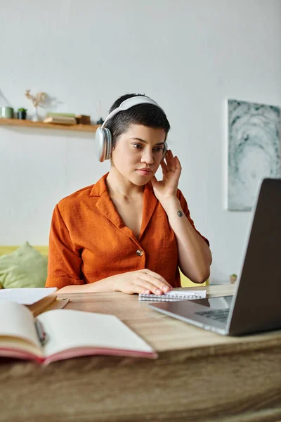 Tiro vertical de estudiante femenina concentrada con auriculares estudiando en su computadora portátil, educación - foto de stock