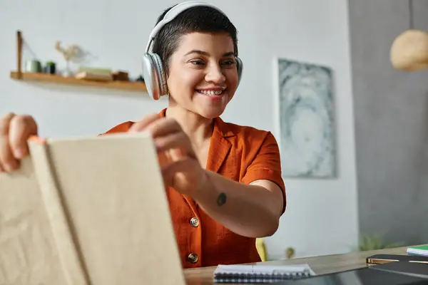Alegre mujer atractiva sosteniendo libro y mirando el ordenador portátil mientras estudia en casa, la educación - foto de stock