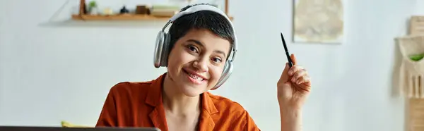 Alegre joven estudiante con auriculares y piercing sonriendo mientras estudia en casa, educación, pancarta - foto de stock