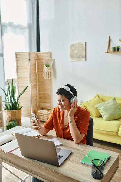 Vertical shot of cheerful young student looking at her phone and touching headphones, education — Stock Photo