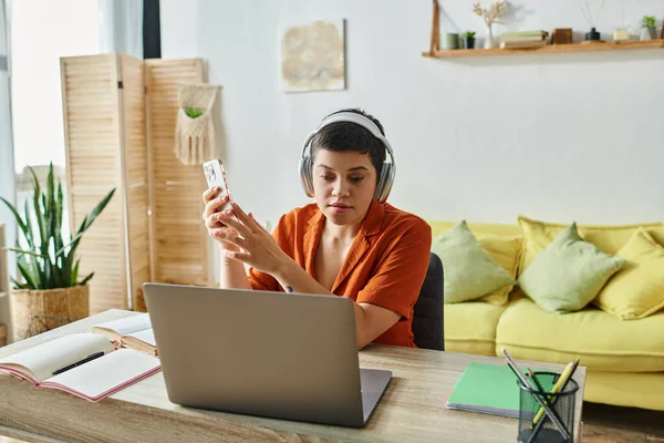 Junge kurzhaarige Frau mit Kopfhörer und Handy, die zu Hause am Laptop lernt, Ausbildung — Stockfoto