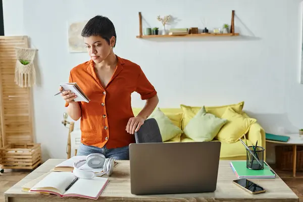 Concentré jeune femme debout près du bureau avec ordinateur portable et papeterie et en regardant ses notes — Photo de stock
