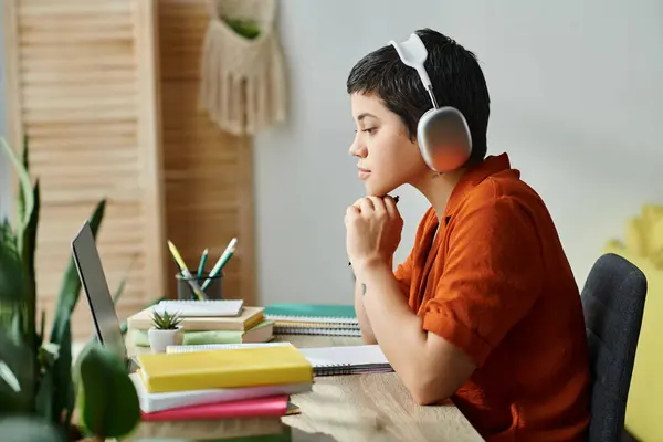 Estudiante trabajadora con auriculares sentados en la mesa estudiando y mirando su computadora portátil, educación - foto de stock