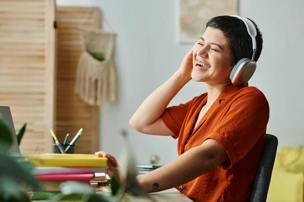 Mujer alegre con auriculares y piercing riendo durante la lección remota, la educación en el hogar - foto de stock
