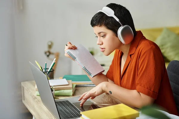 Joven estudiante en traje casual con tatuaje estudiando en la computadora portátil sosteniendo notas, educación - foto de stock