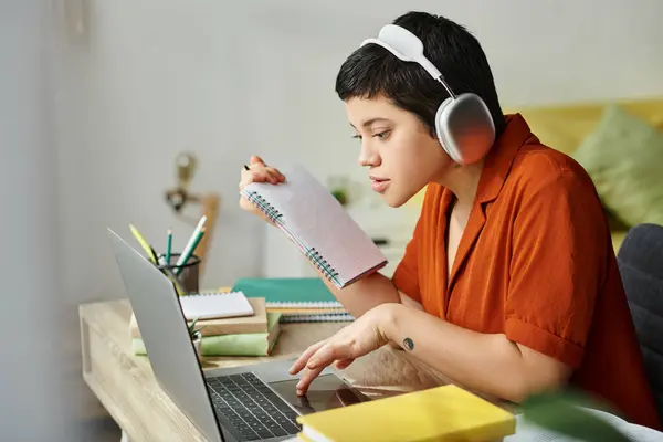 Joven estudiante en traje casual con tatuaje estudiando en la computadora portátil sosteniendo notas, educación - foto de stock