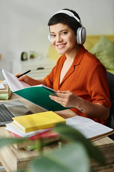 Vertical shot of attractive young woman looking at camera while studying and holding textbook — Stock Photo