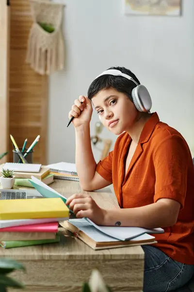 Tiro vertical de la joven estudiante rodeada de materiales de estudio sentado en el escritorio, la educación - foto de stock