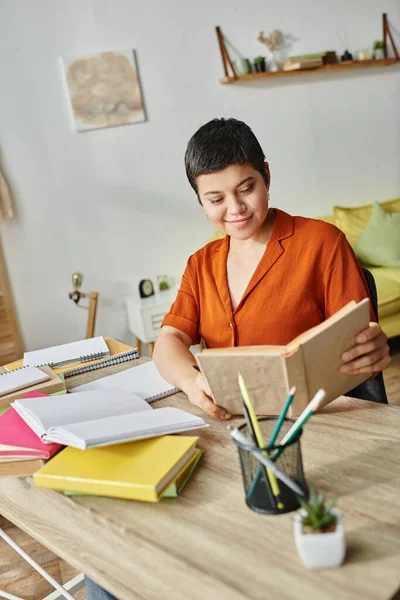 Plan vertical de la jeune femme joyeuse regardant le manuel tout en étudiant à la maison, l'éducation à la maison — Photo de stock