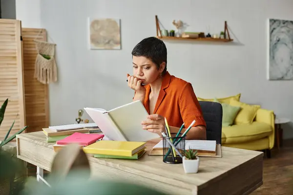 Jeune étudiante réfléchie assise au bureau et étudiant son matériel avec stylo à la main, éducation — Photo de stock