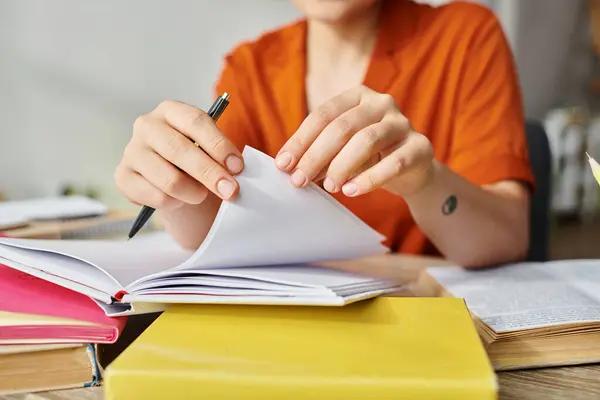 Vue recadrée du jeune étudiant avec tatouage en chemise orange tournant pages de manuels, étudiant de la maison — Photo de stock