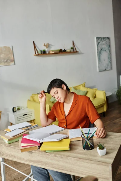 Plano vertical del estudiante cansado trabajador que se sienta en el escritorio con la pluma en el libro de texto de la lectura de la mano - foto de stock