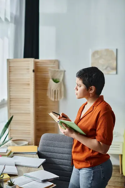 Vertical shot of serious concentrated woman posing in profile holding book and pen, looking away — Stock Photo