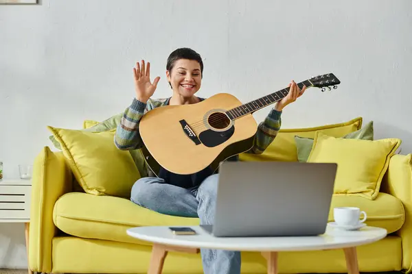Alegre joven mujer asistir a la lección de guitarra en línea y saludar a la cámara portátil, la educación en casa - foto de stock