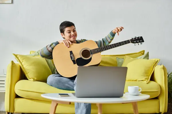 Young jolly woman in casual attire sitting on sofa learning how to play guitar on remote class — Stock Photo