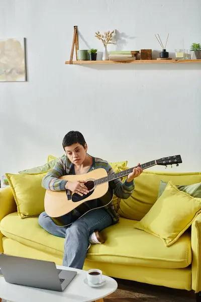 Plan vertical de jeune femme concentrée assise sur un canapé avec guitare assistant à une leçon de musique en ligne — Photo de stock
