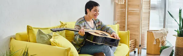 Mujer de pelo corto feliz sosteniendo la guitarra durante la lección de música remota, educación en casa, pancarta - foto de stock