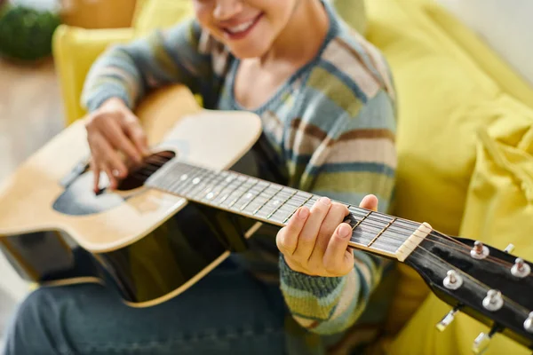 Recortado vista de sonriente mujer joven en traje casual aprender a tocar la guitarra en la lección remota - foto de stock