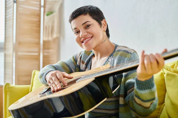 Sonriente joven con atuendo casual asistiendo a la lección de guitarra remota y sonriendo a la cámara, educación - foto de stock