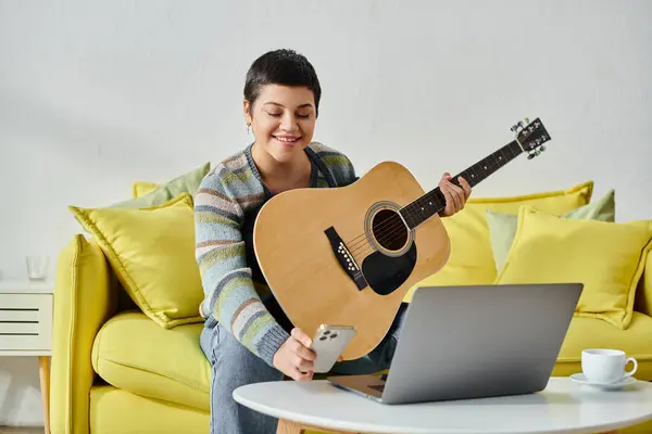 Cheerful attractive woman looking at her phone during remote guitar lesson, education at home — Stock Photo