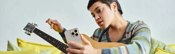 Atractiva mujer enfocada que asiste a clases de guitarra en línea con teléfono en las manos, educación, bandera - foto de stock