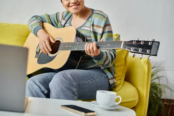 Vista recortada de la joven sentada frente a la computadora portátil aprendiendo a tocar la guitarra en clase remota - foto de stock