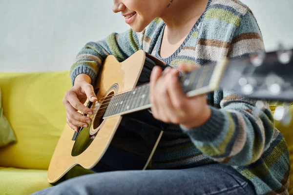 Vista recortada de mujer joven con piercing y tatuaje aprendiendo a tocar la guitarra, clase remota - foto de stock