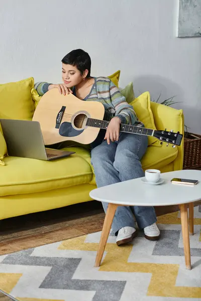 Vertikale Aufnahme einer fröhlichen jungen Frau, die mit Gitarre auf dem Sofa sitzt, während sie ferngesteuerten Musikunterricht nimmt, Bildung — Stockfoto