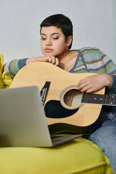 Tiro vertical de mujer atractiva joven que asiste a la lección de guitarra en línea sentado en el sofá, la educación - foto de stock