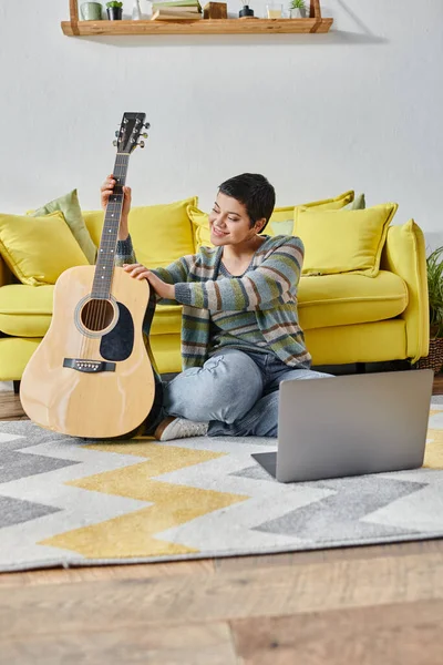 Vertical shot of attractive woman with short hair smiling cheerfully at online guitar lesson — Stock Photo